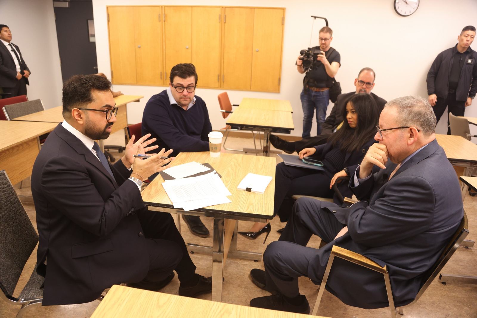 Principals in a working briefing with a broadcast camera operator behind them